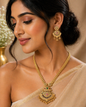 Vellorene gold tone temple pendant necklace set with matching earrings displayed on black stand